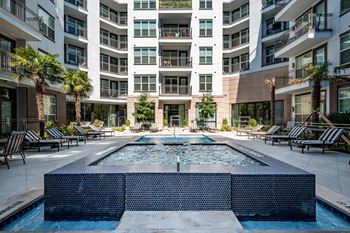 A large pool in the middle of a courtyard surrounded by lounge chairs and palm trees.